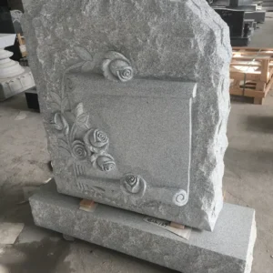 a gray tombstone carved with roses and a scroll‌